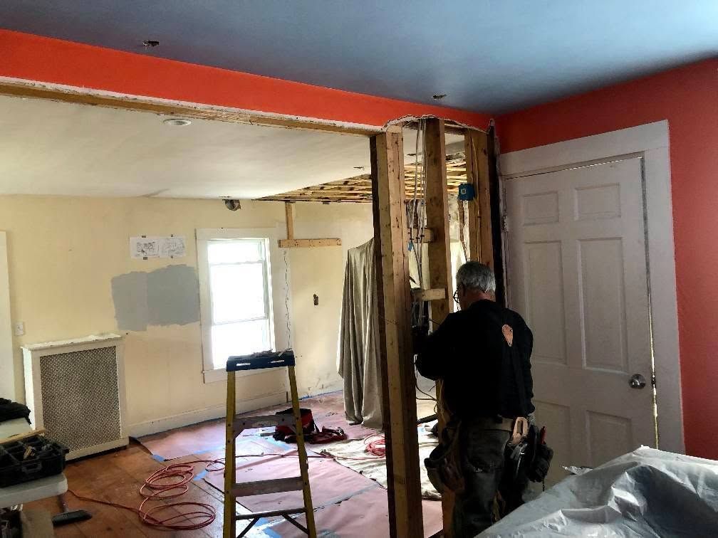 Worker frames a doorway in a partially demolished room with exposed studs and debris.