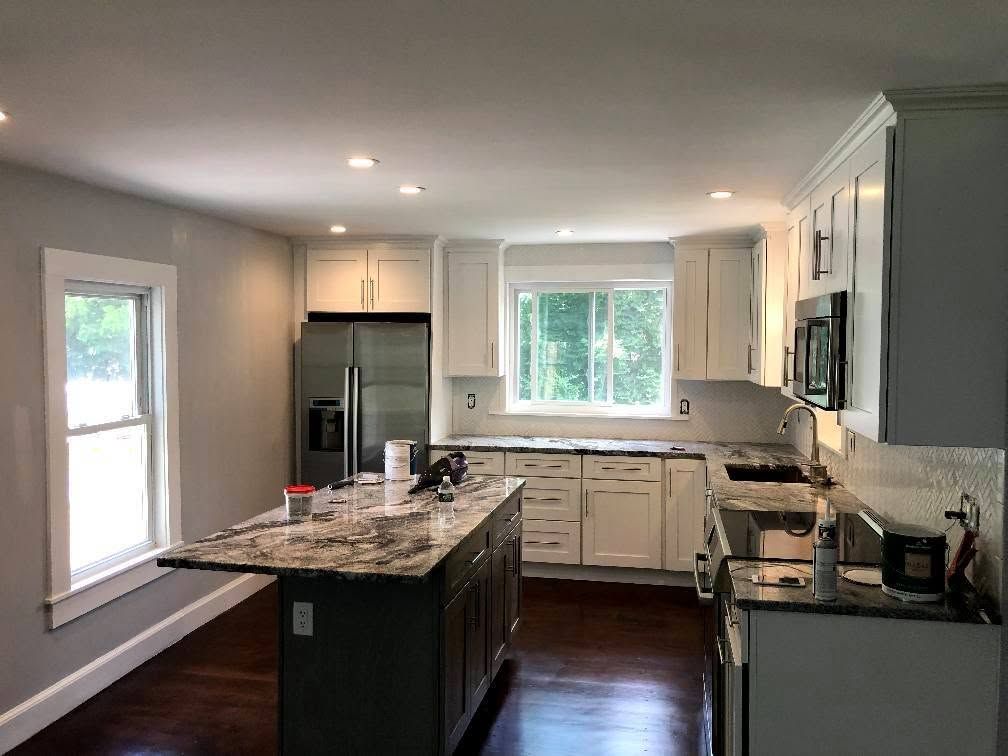 Modern kitchen with dark island, white cabinets, stainless fridge, and large window