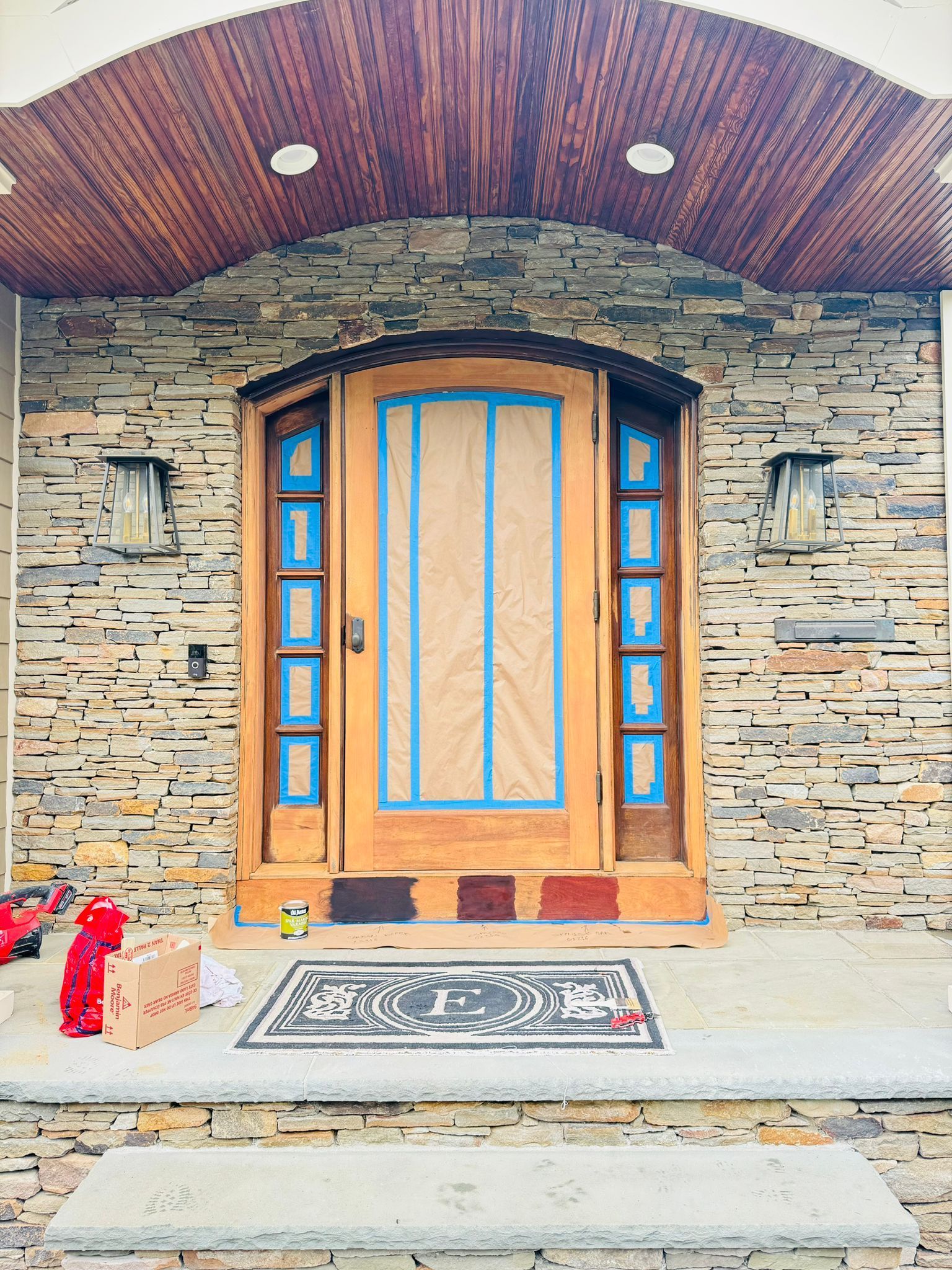 Stone house entrance with arched wooden door, blue window accents, and decorative rugs on the porch