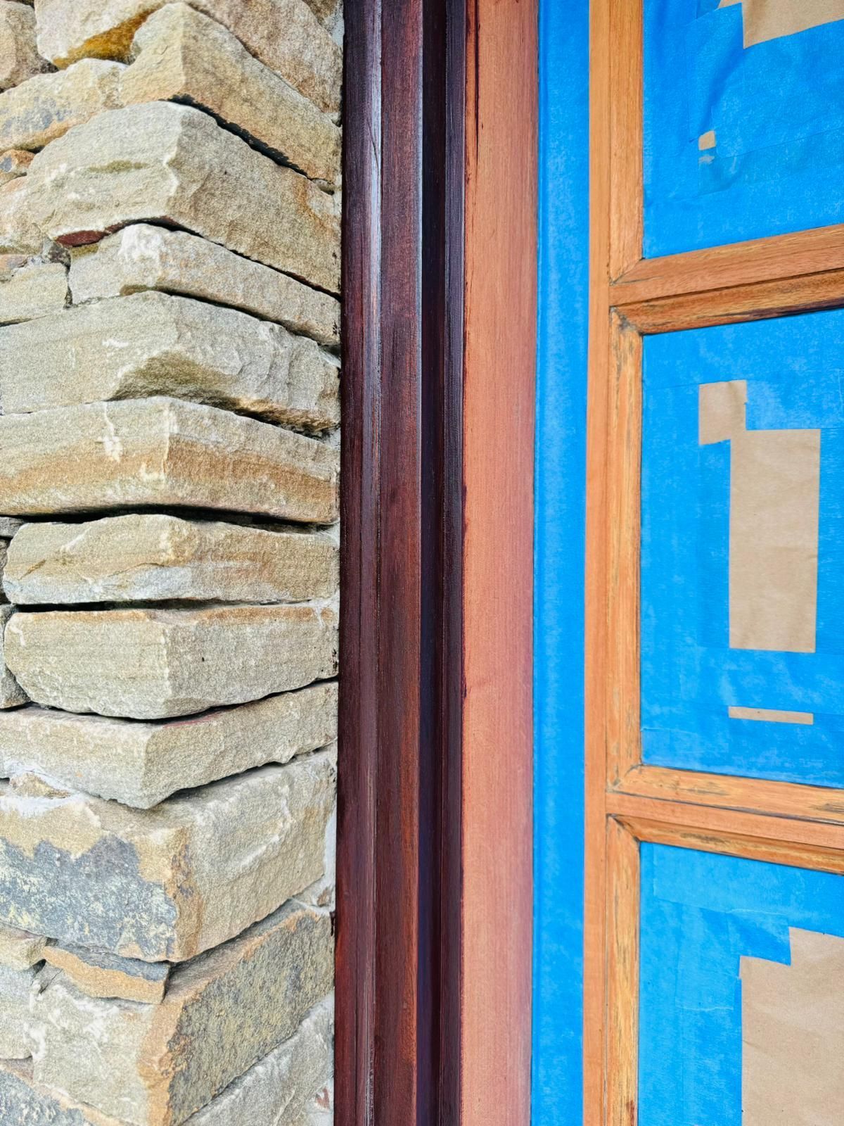 Stone wall next to a wooden-framed blue window with taped paper on the glass