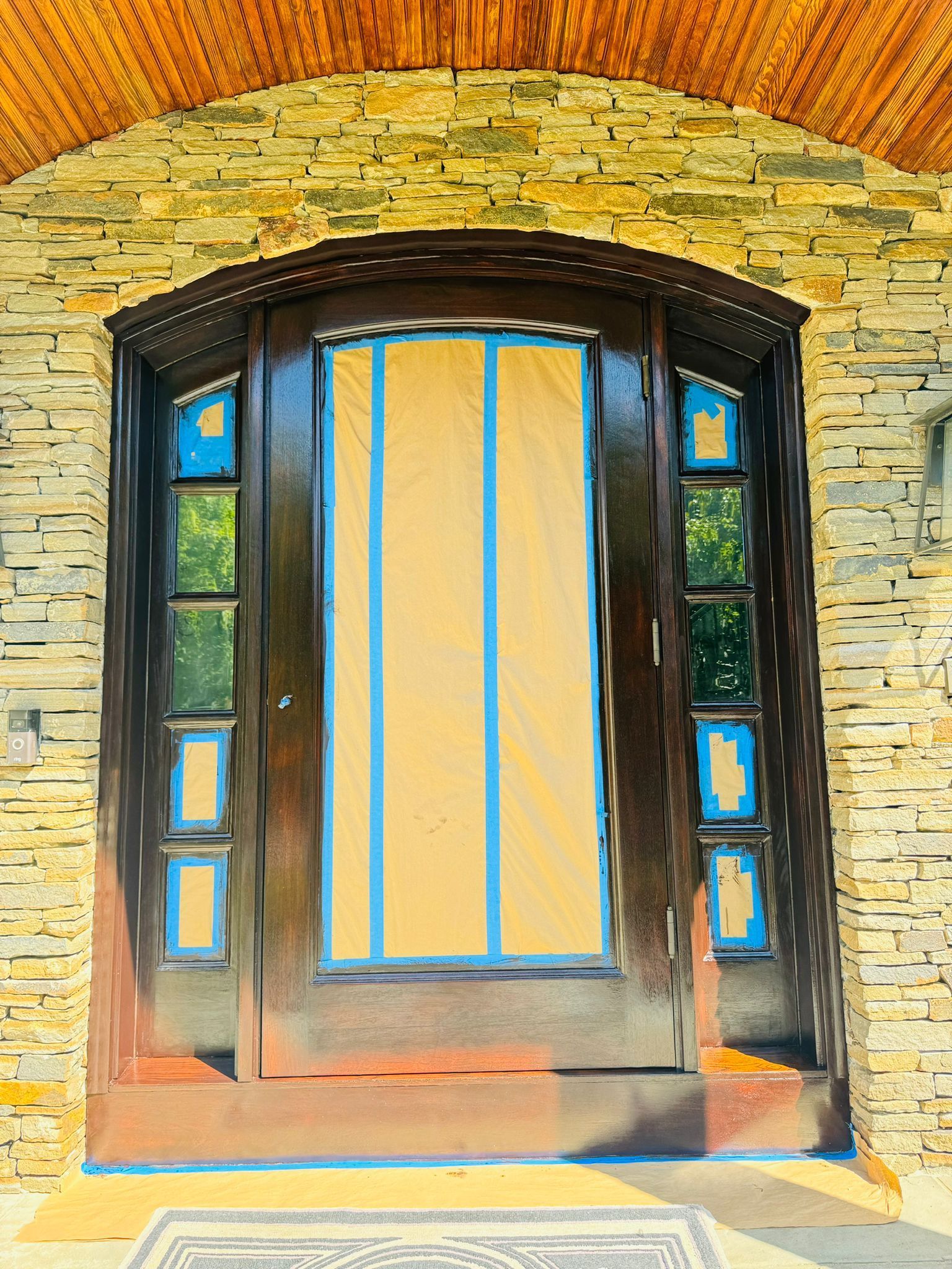 Brick house front door with arched stone surround and blue-taped glass panels