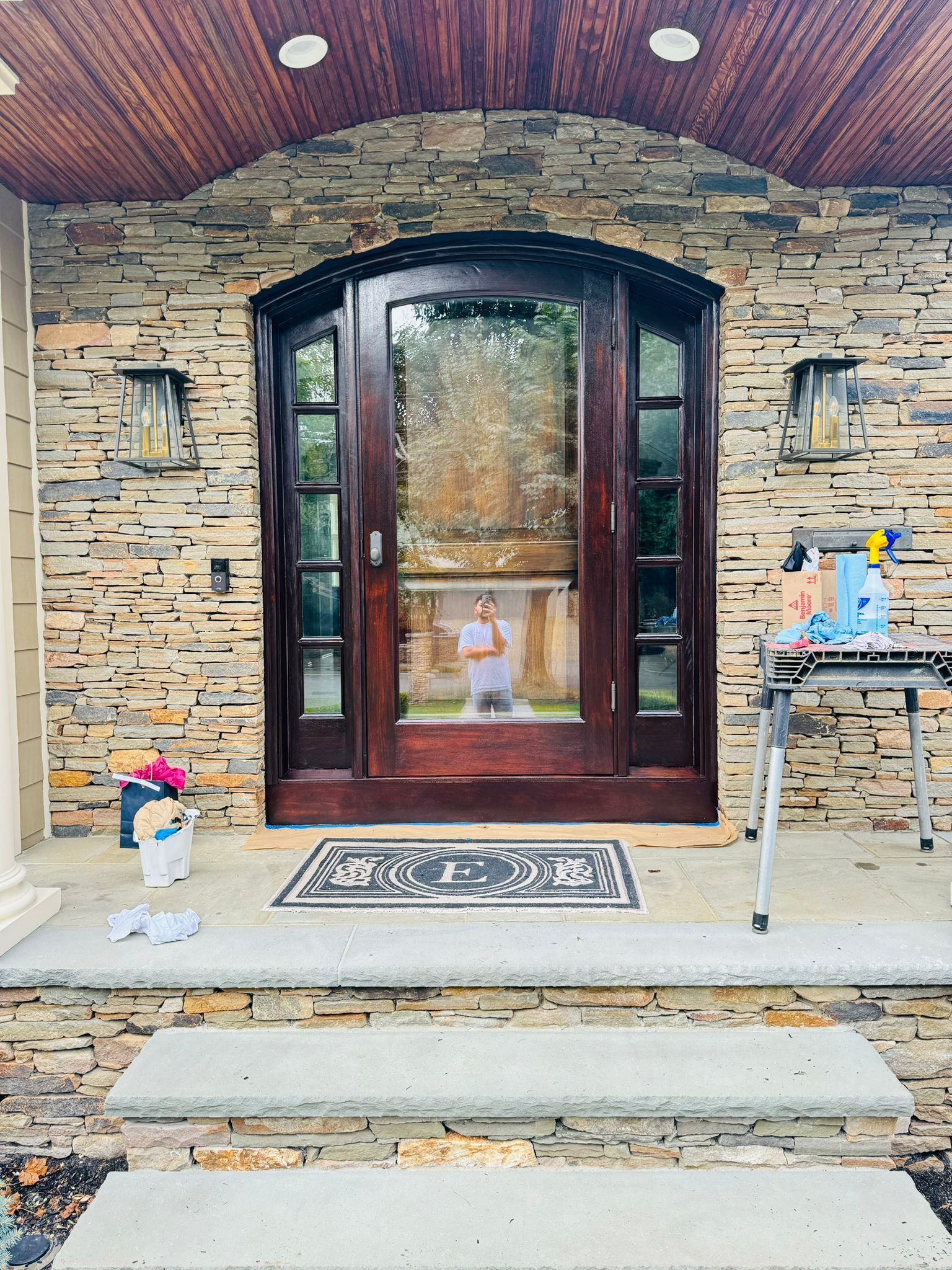 Front porch with stone siding, dark wooden double doors, and a small rug and table decoration.
