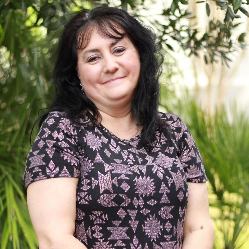 Woman with dark hair and a patterned black shirt, smiling outdoors.