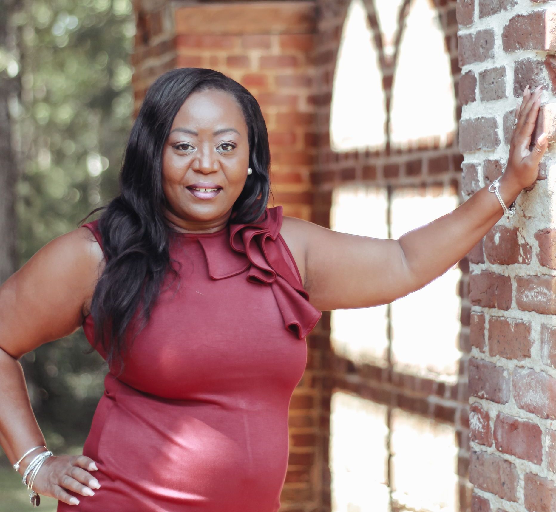 Woman in a burgundy dress leaning against a brick wall, smiling at the camera.