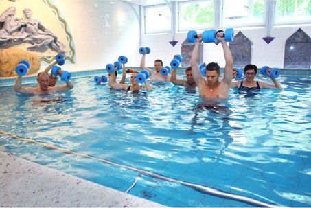Menschen bei der Wassergymnastik in einem Schwimmbecken. Sie arbeiten mit blauen Gewichten.