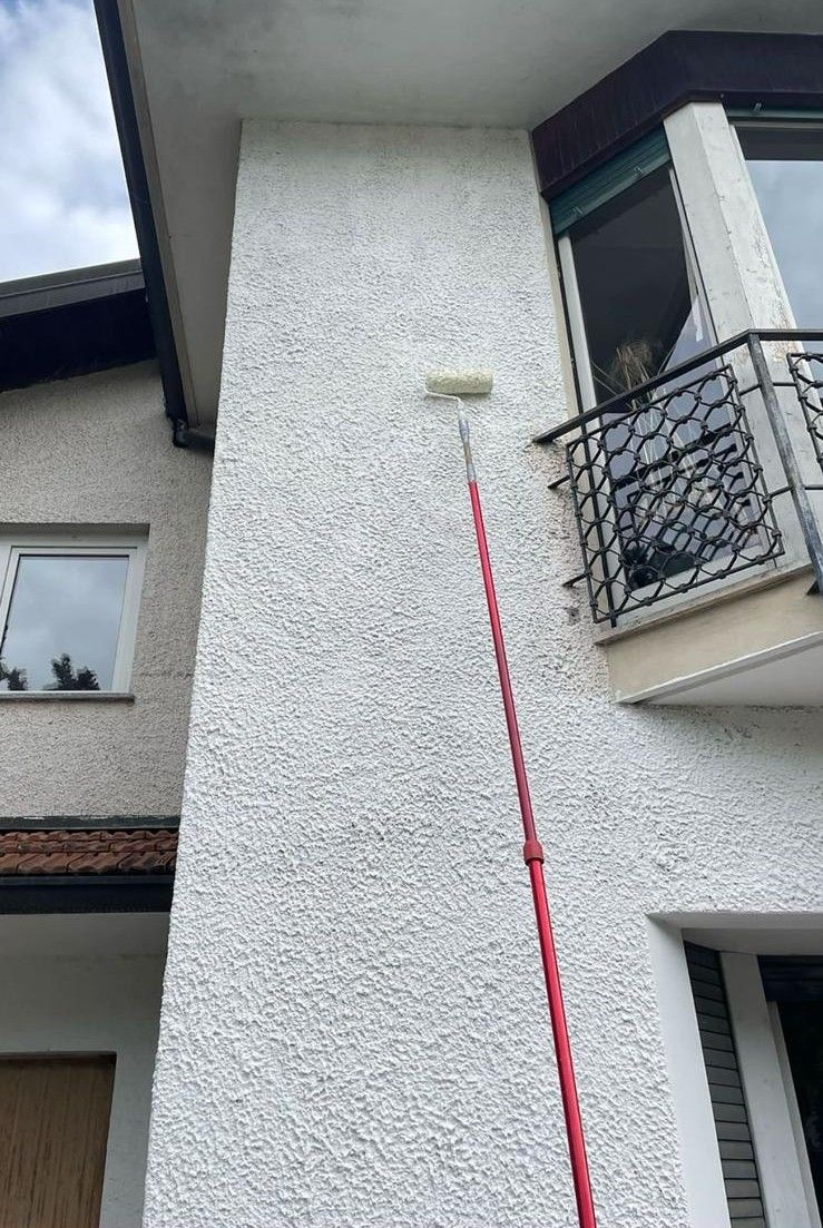 Muro esterno in stucco bianco con balcone e una linea verticale rossa che punta verso un punto vicino alla sommità.