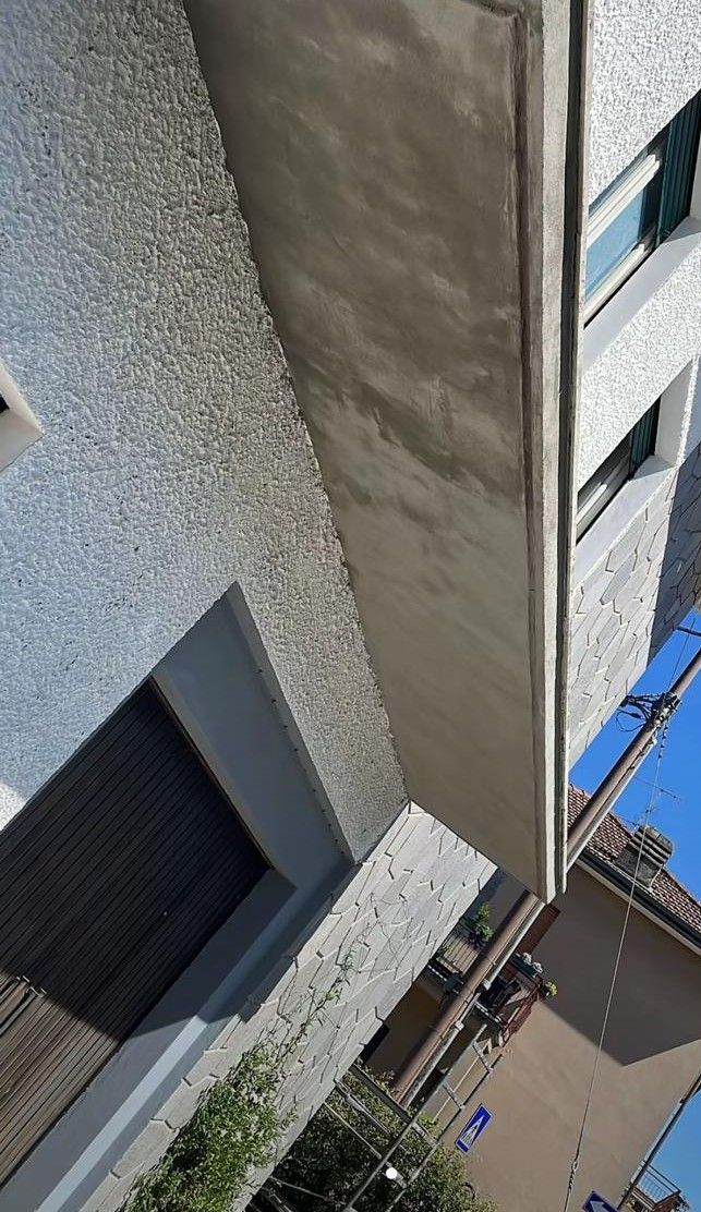 Vista inclinata dell'esterno di un condominio con finestre, muri in stucco e cielo azzurro sopra.