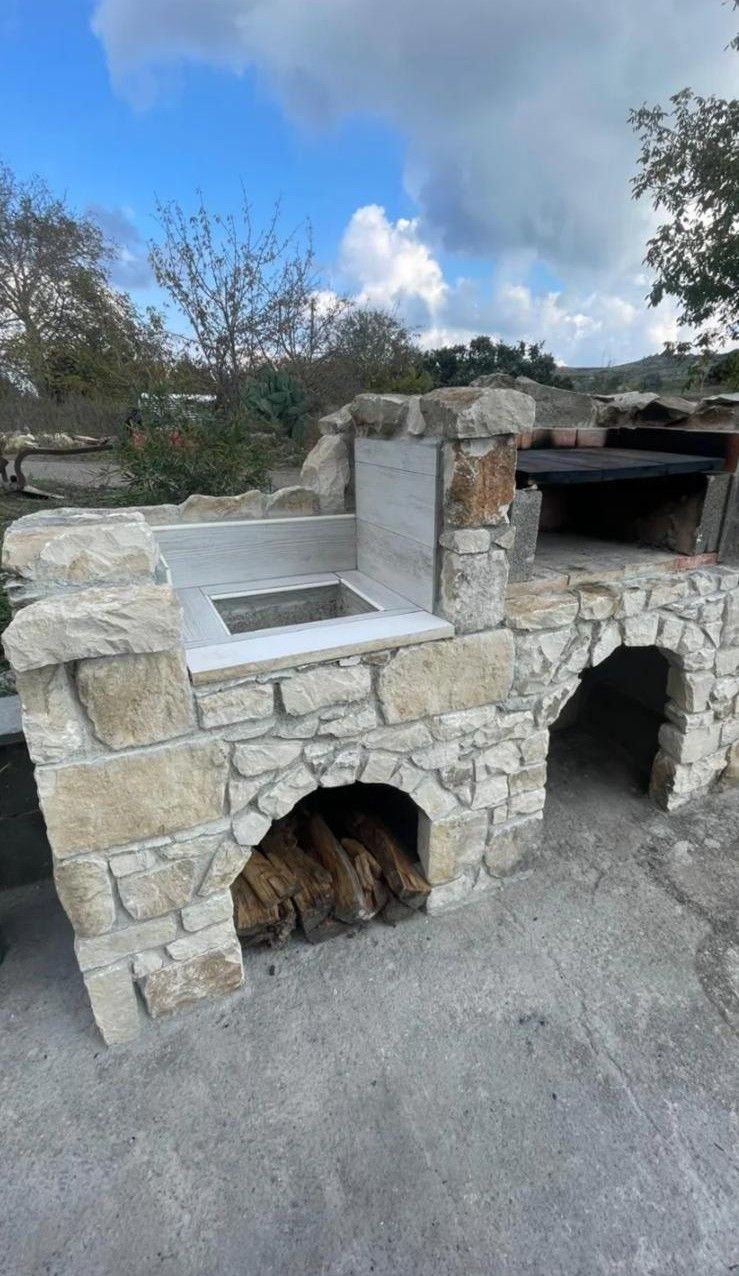 Barbecue in pietra da esterno con forno integrato e aperture ad arco contro un cielo nuvoloso