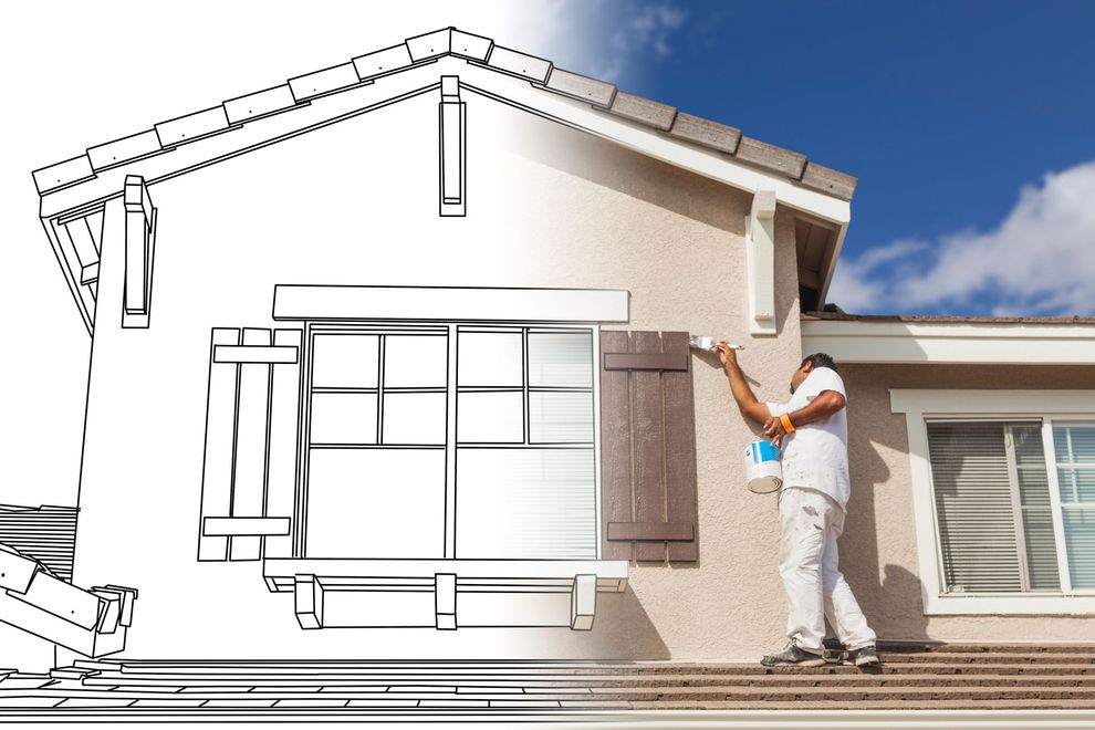 Un operaio dipinge la parete esterna di una casa con un primer bianco, delineando il tetto e le finestre con una matita nera.