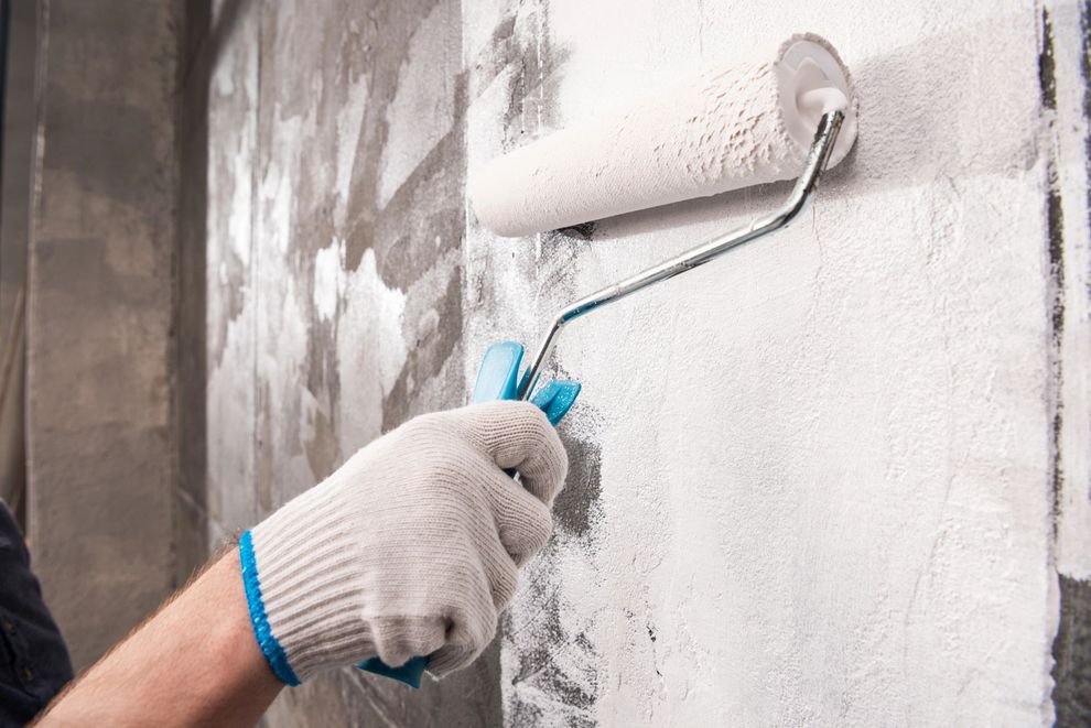 Mano guantata che dipinge un muro di bianco con un rullo da pittura