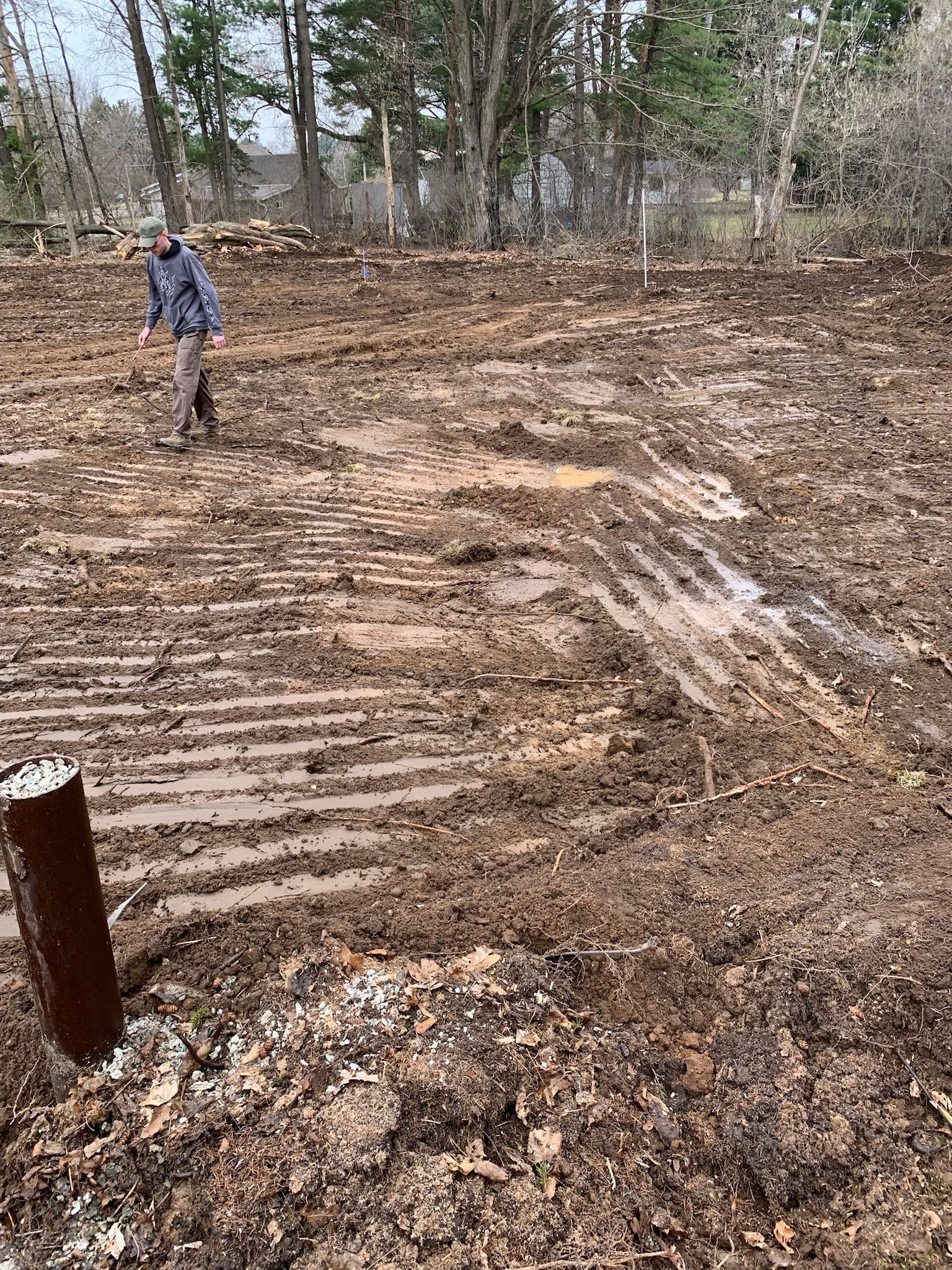 Muddy construction site with tire tracks and a person walking in the distance.