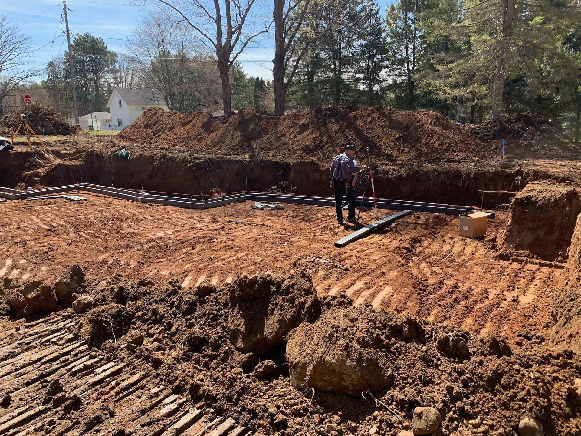 Construction site with a person working on laying pipes in a trench, dirt and trees in background.