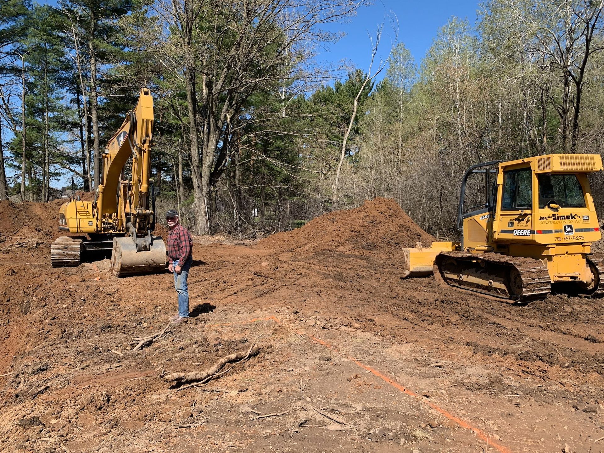 Construction site with excavator and bulldozer; a person standing nearby.