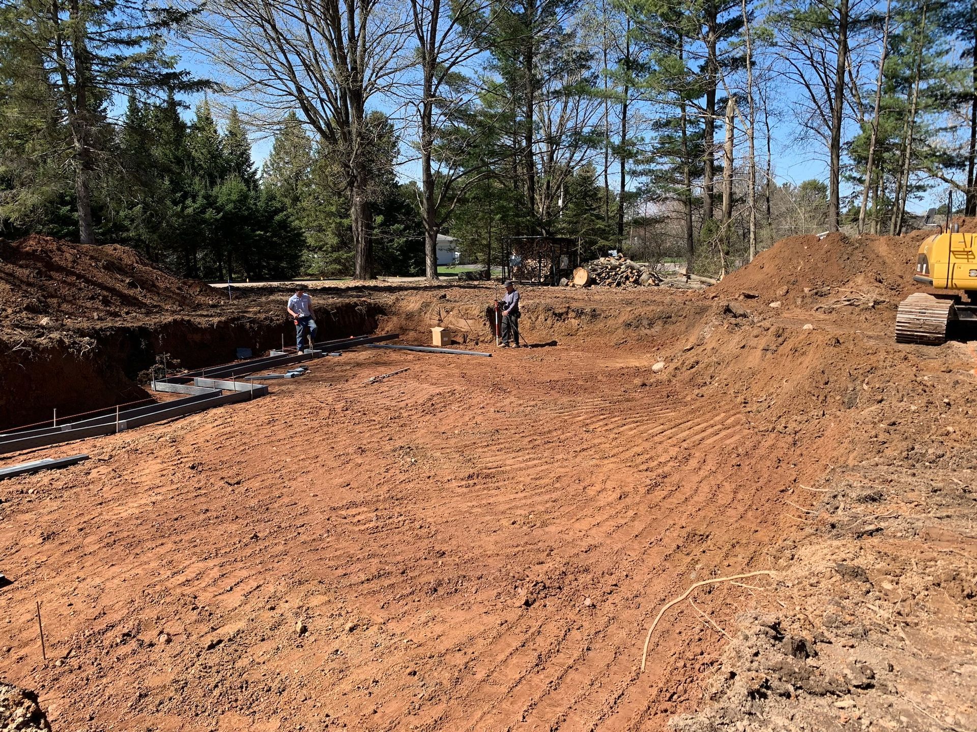 Construction site, cleared dirt with equipment, workers, trees in background, sunny day.