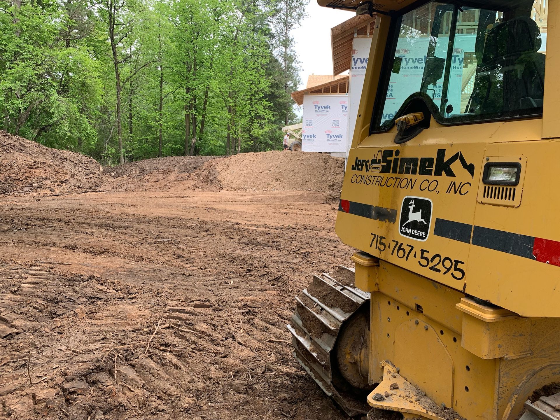 A yellow bulldozer on a construction site, grading dirt. Building in background.
