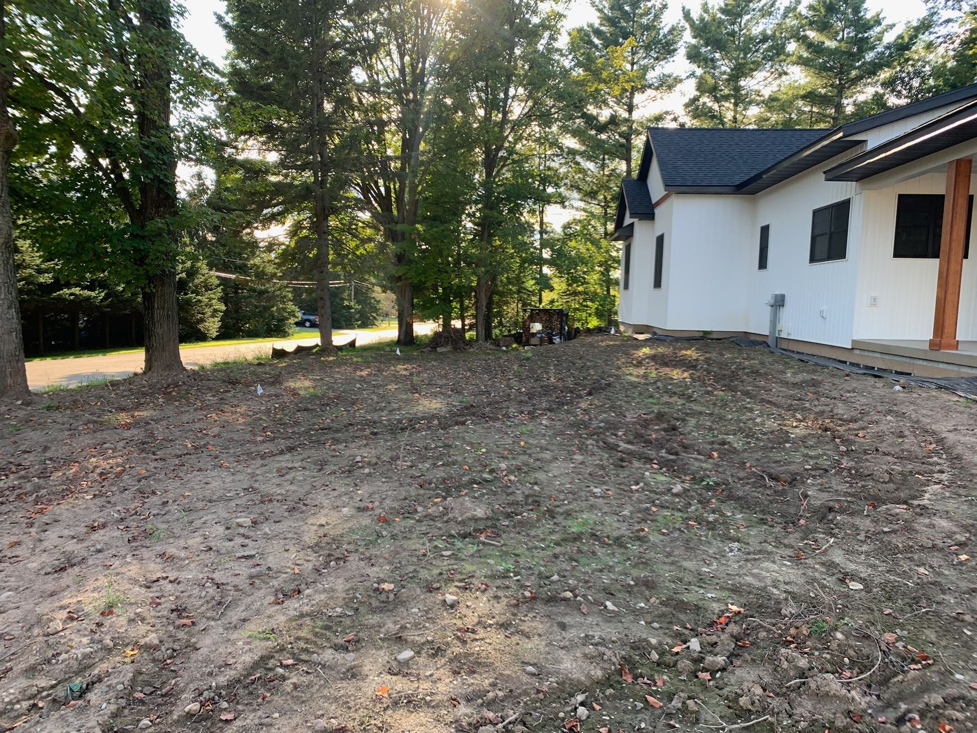 A house with a cleared front yard. Brown dirt, trees in the background, sunlight.