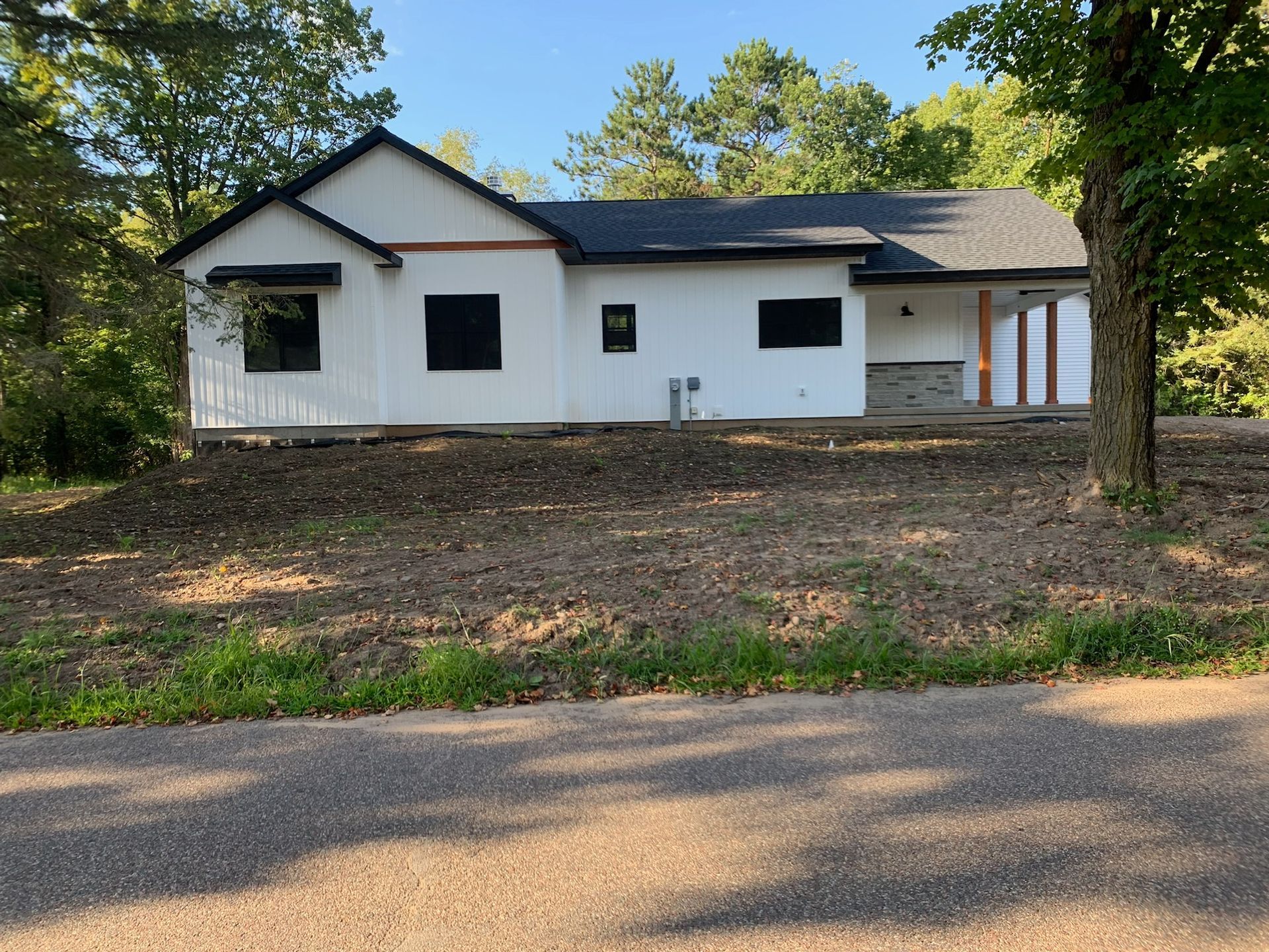 White house with black trim, windows, and roof on a brown grassy hill next to a road and trees.