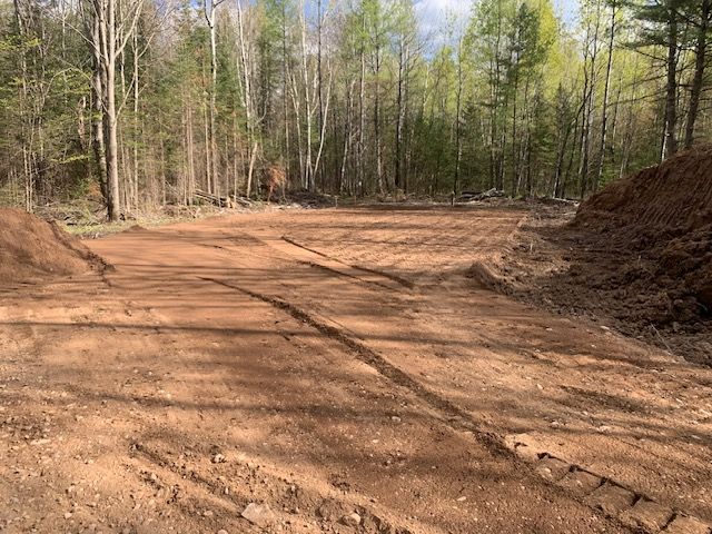 Cleared dirt area with tire tracks and pile of dirt, surrounded by a forest.