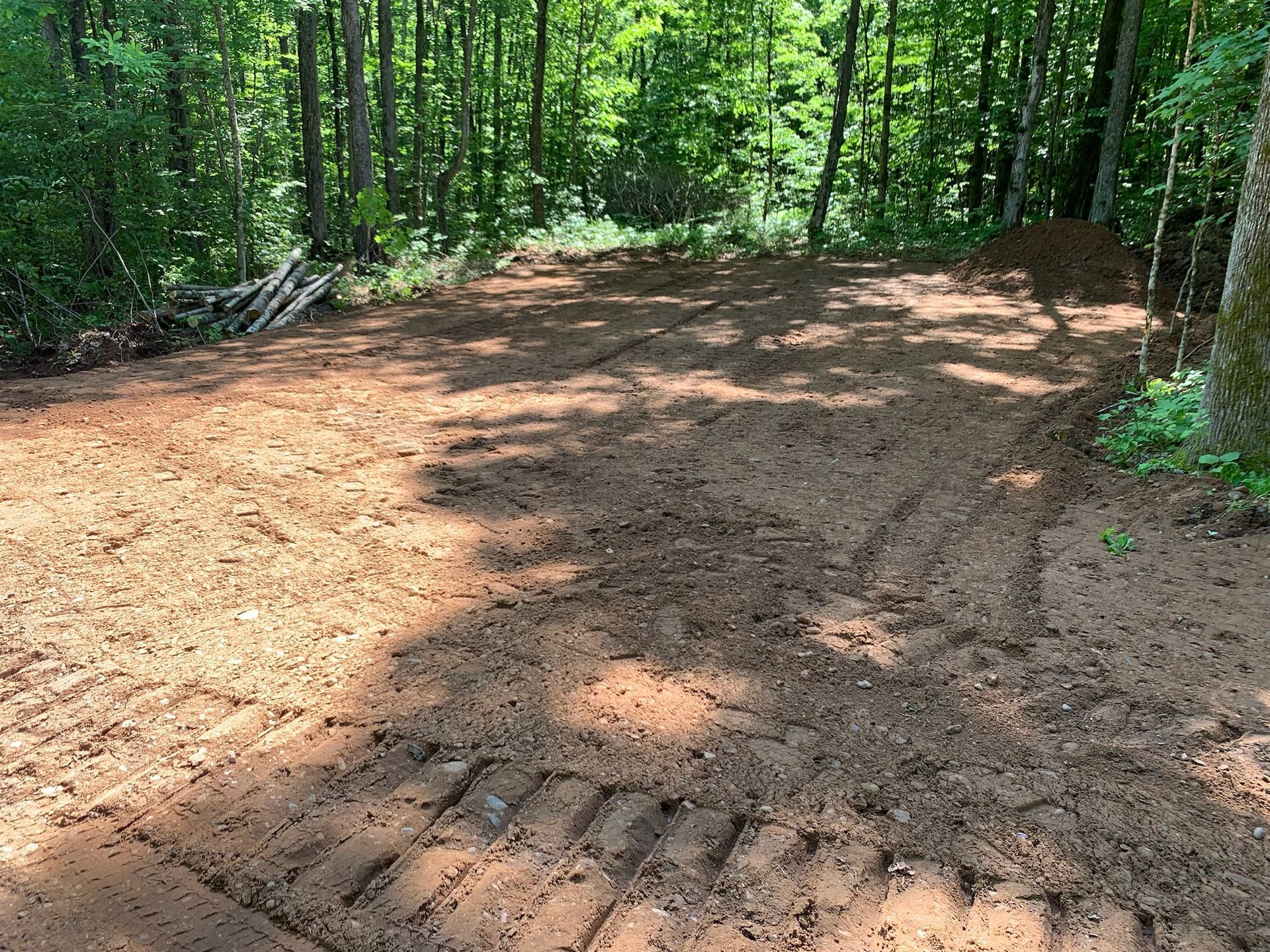 Dirt clearing in a forest, marked with tire tracks, possibly for construction.
