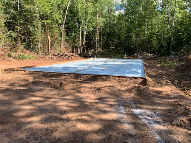 Concrete foundation in a clearing, surrounded by dirt and trees.