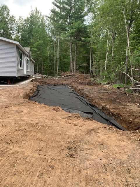 Excavated area with black fabric lining, next to a house and trees.