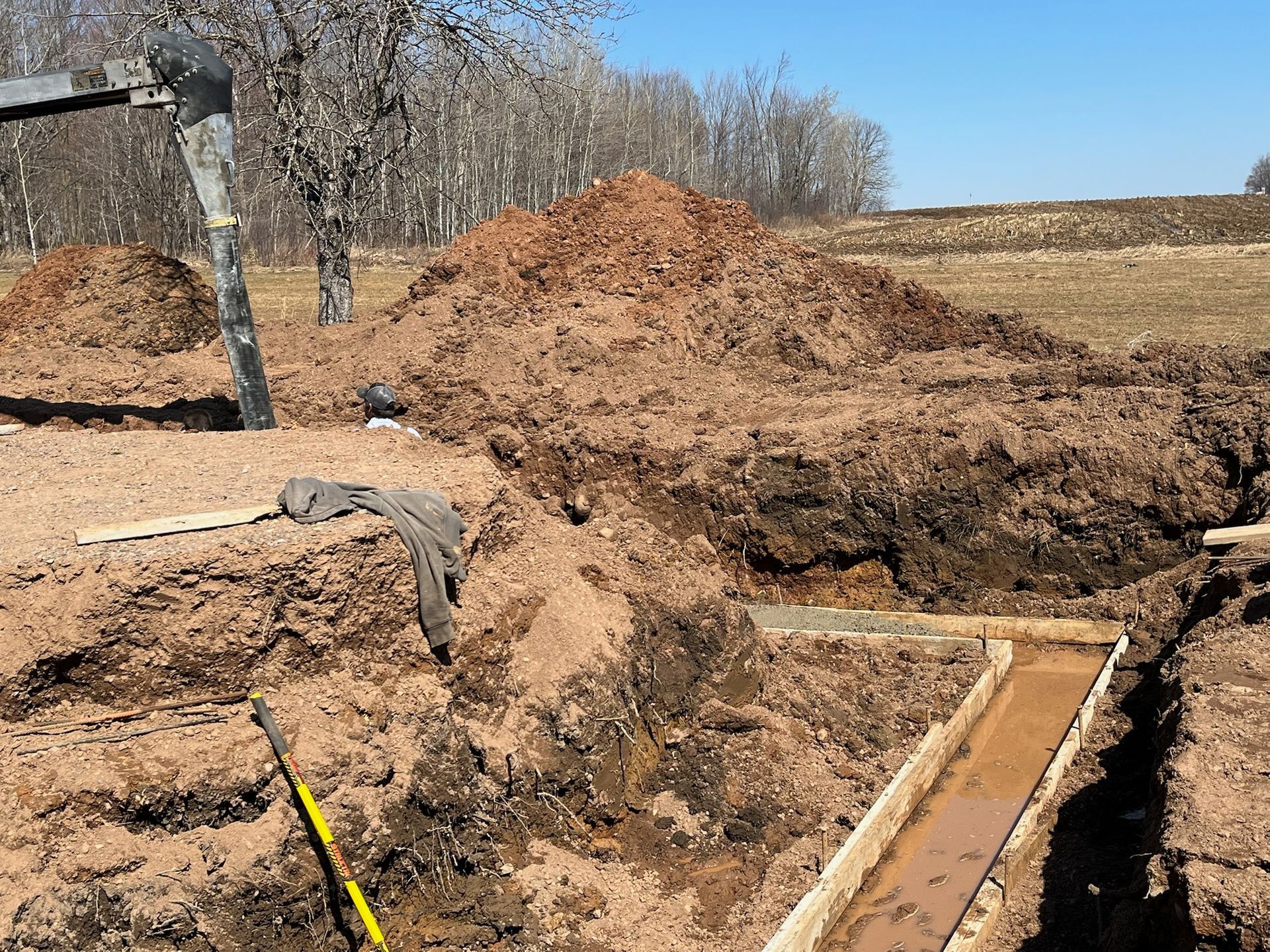 Construction site with excavated trench, dirt pile, and wooden forms.