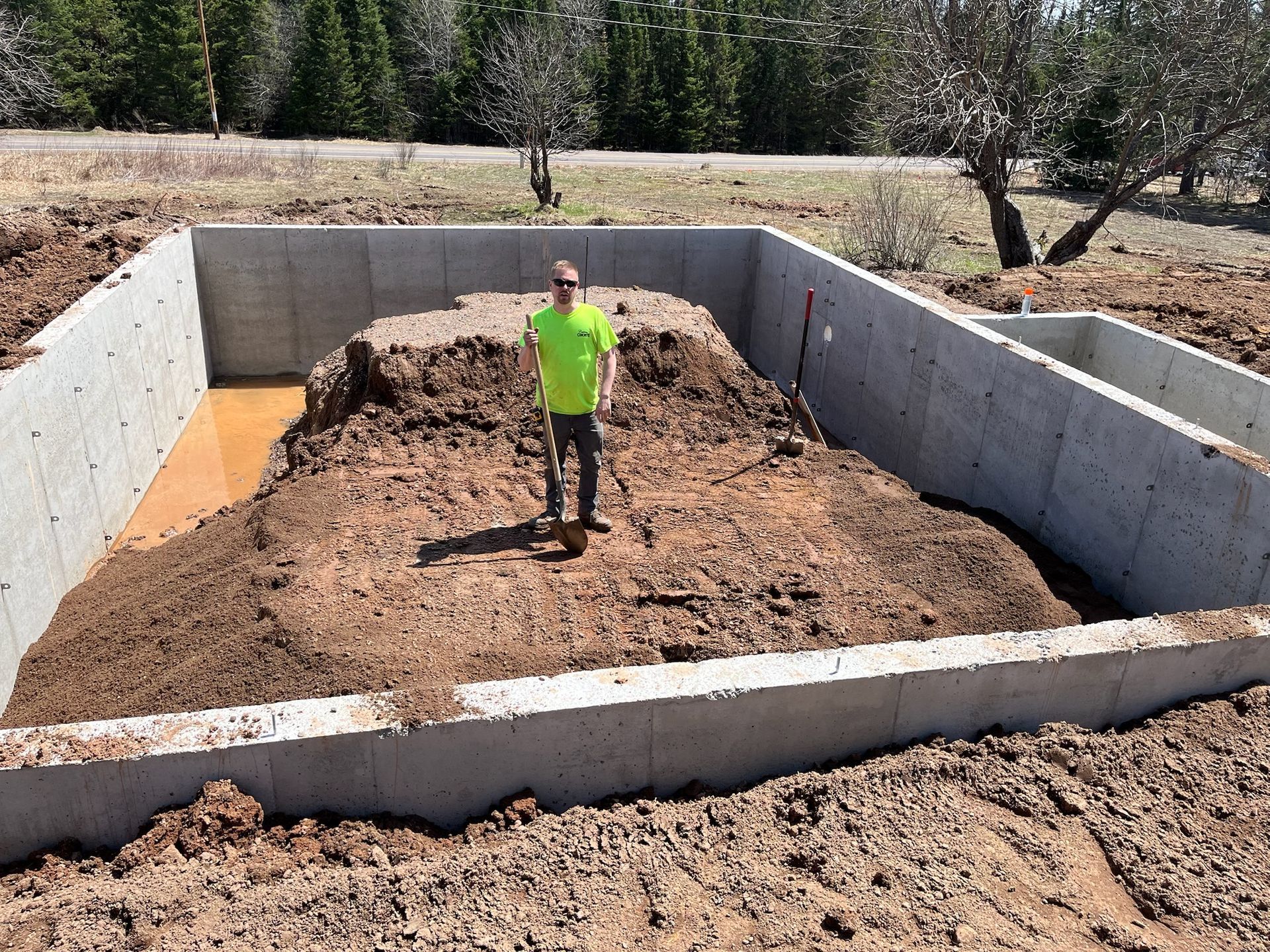 Person standing in a concrete foundation filled with dirt. Outdoors, sunny.