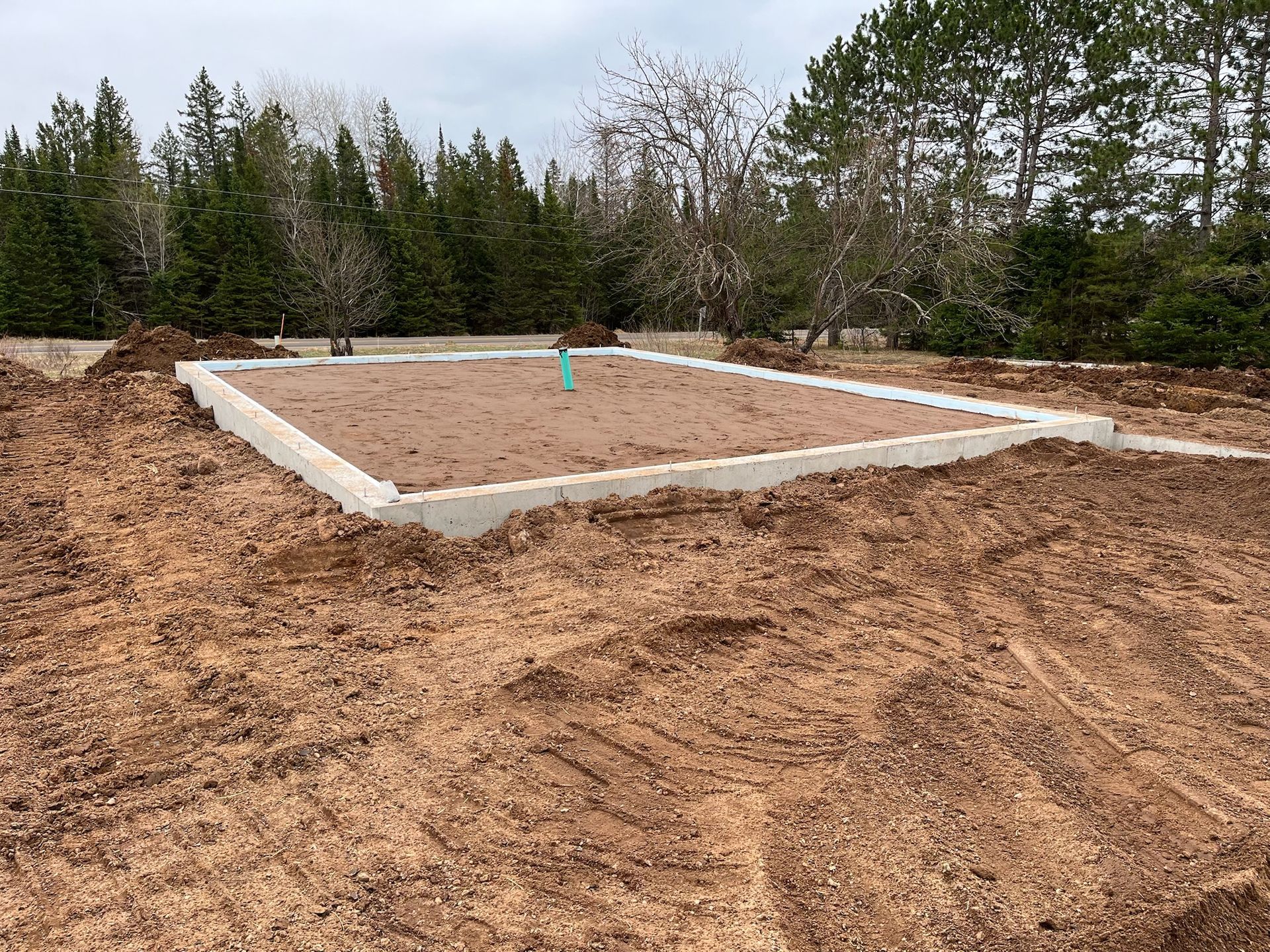 Concrete foundation for a building in a dirt lot, with trees in the background.