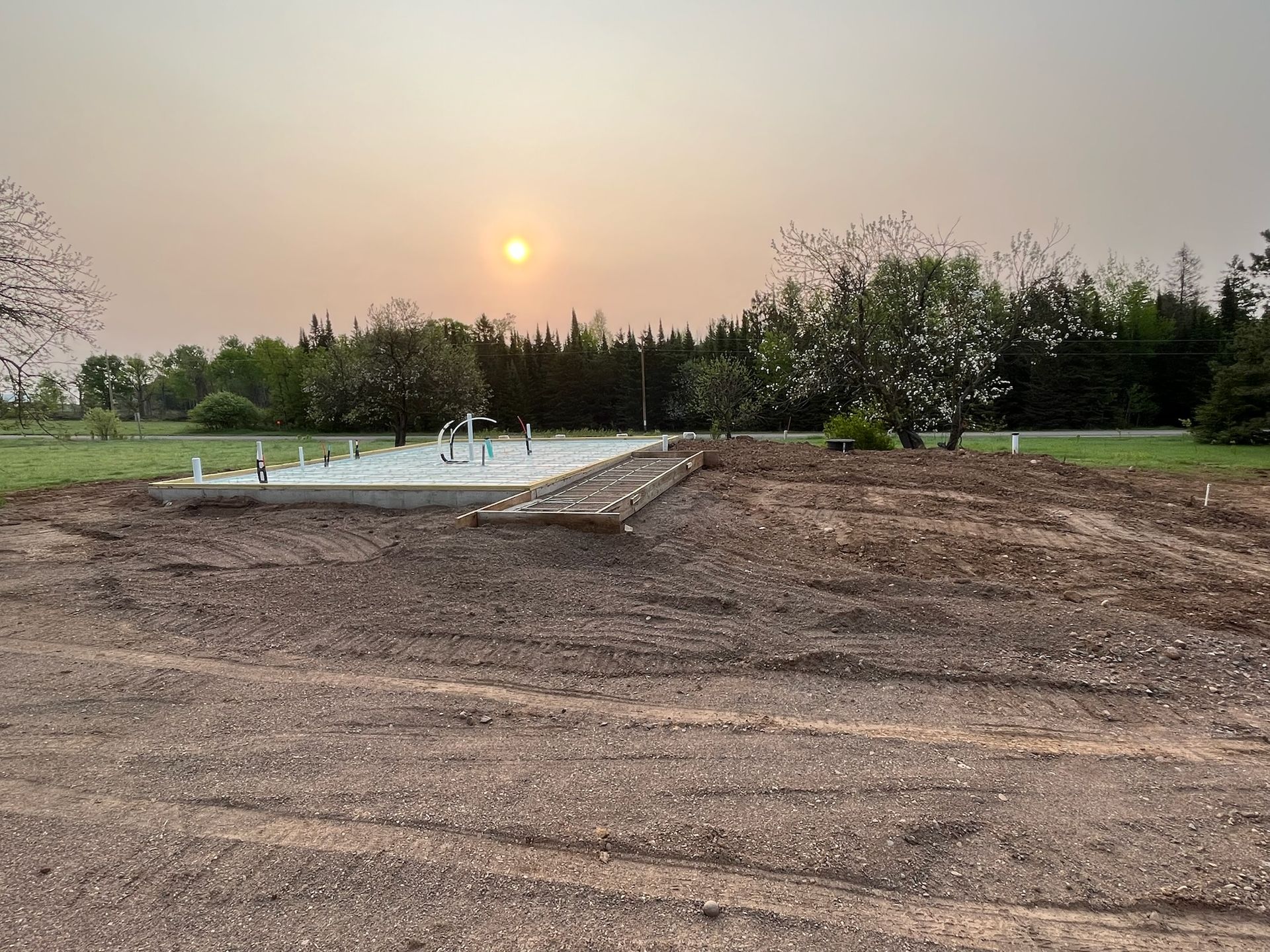 Construction site with gravel, concrete base, and plumbing. Sunset in the background.