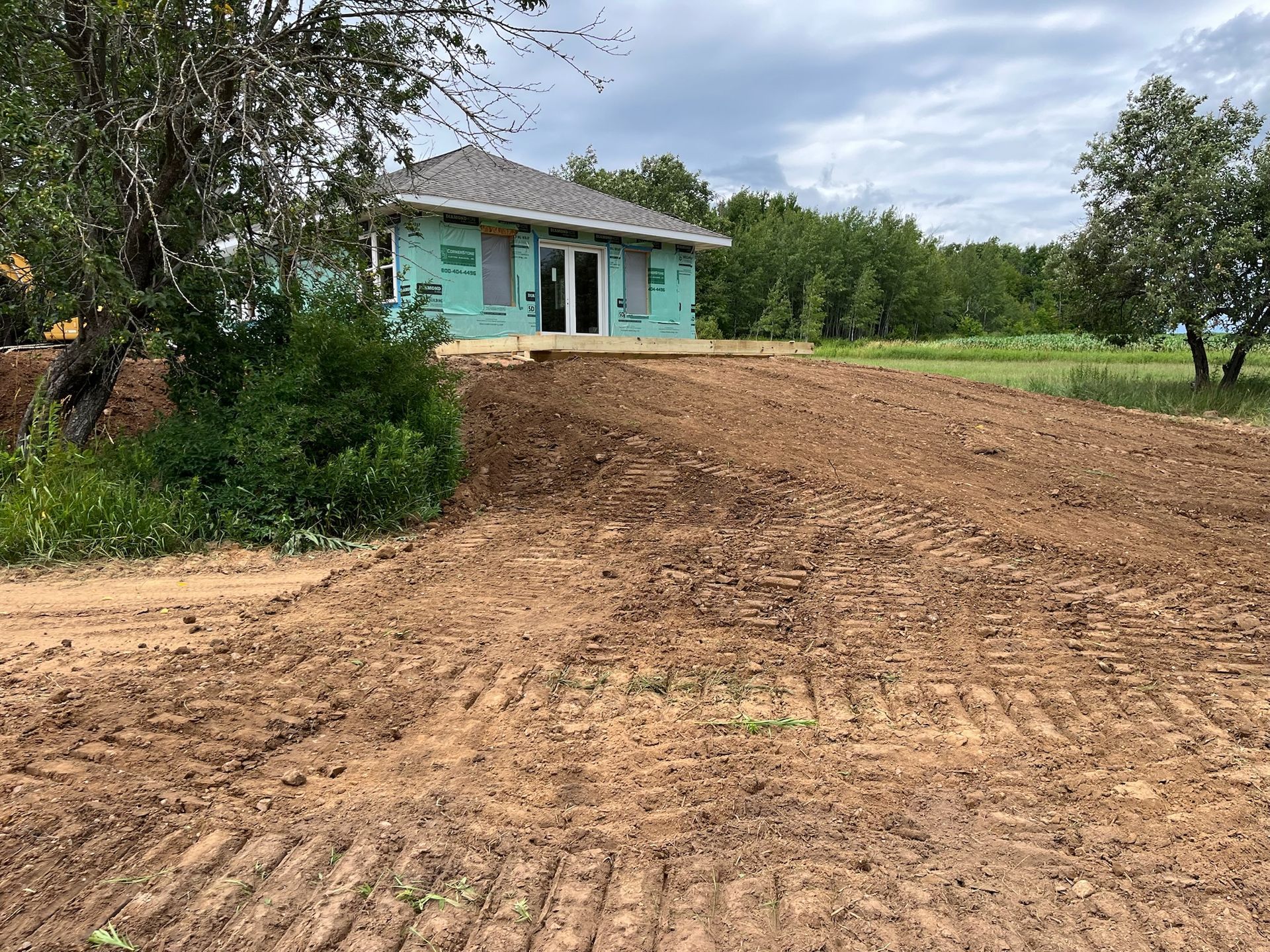 Small building under construction, with green wrap, on a graded dirt lot.