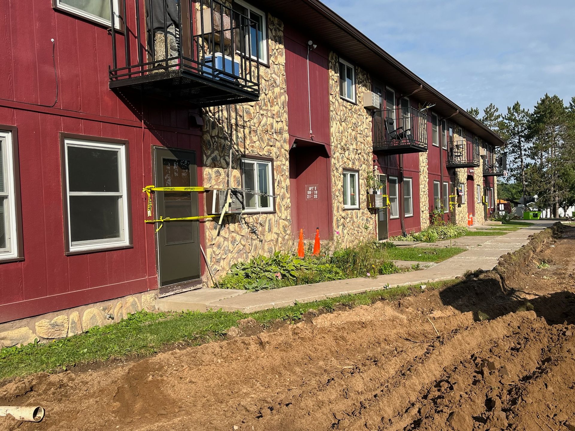 Apartment building with maroon siding and stone accents; construction site in front.