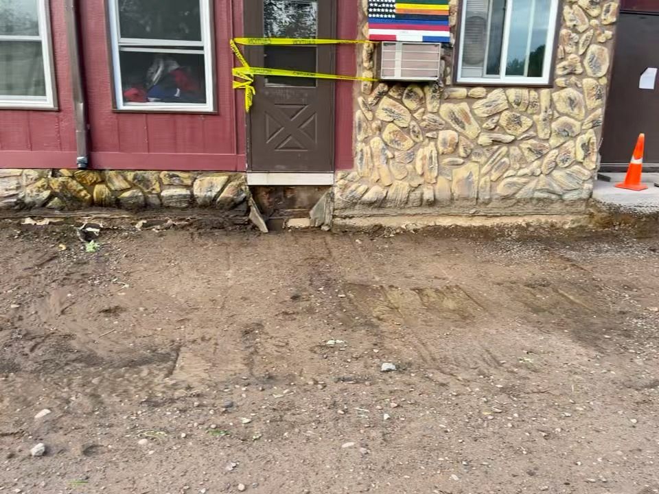 Exterior of a building with a dirt patch. Yellow caution tape blocks a door.