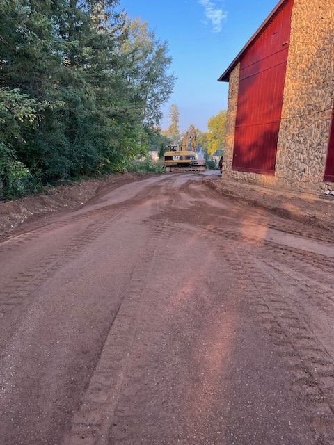 Dirt road leading to a red barn. A bulldozer is on the road near trees on the left.