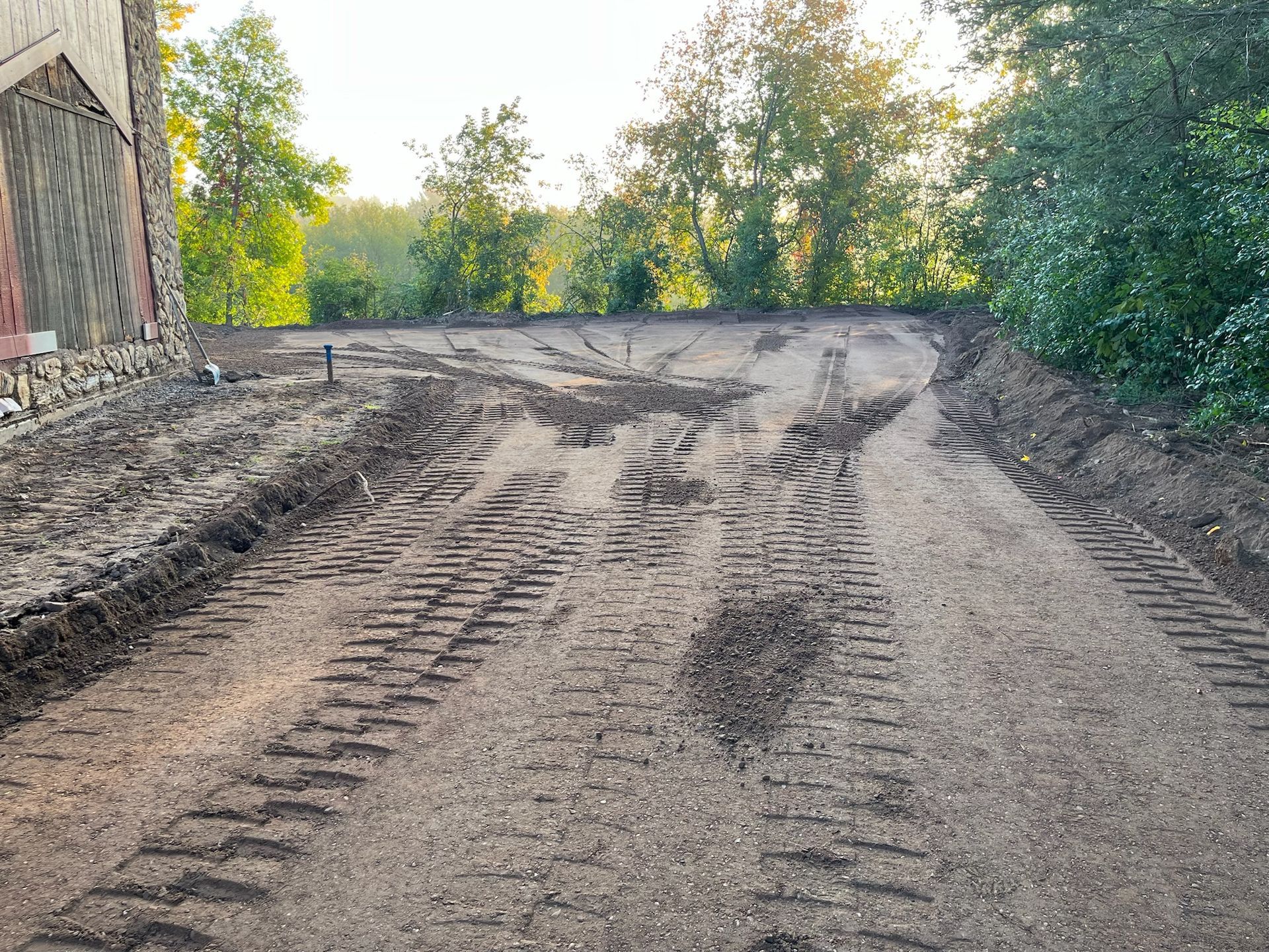 Dirt road with tire tracks, leading toward trees and a building.
