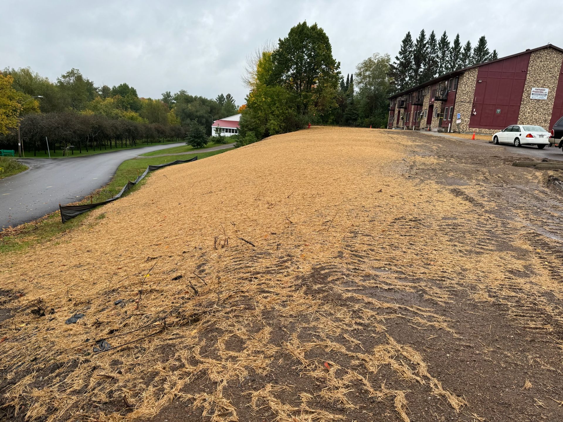 A large pile of straw on a slope next to a road and a building with a red facade.