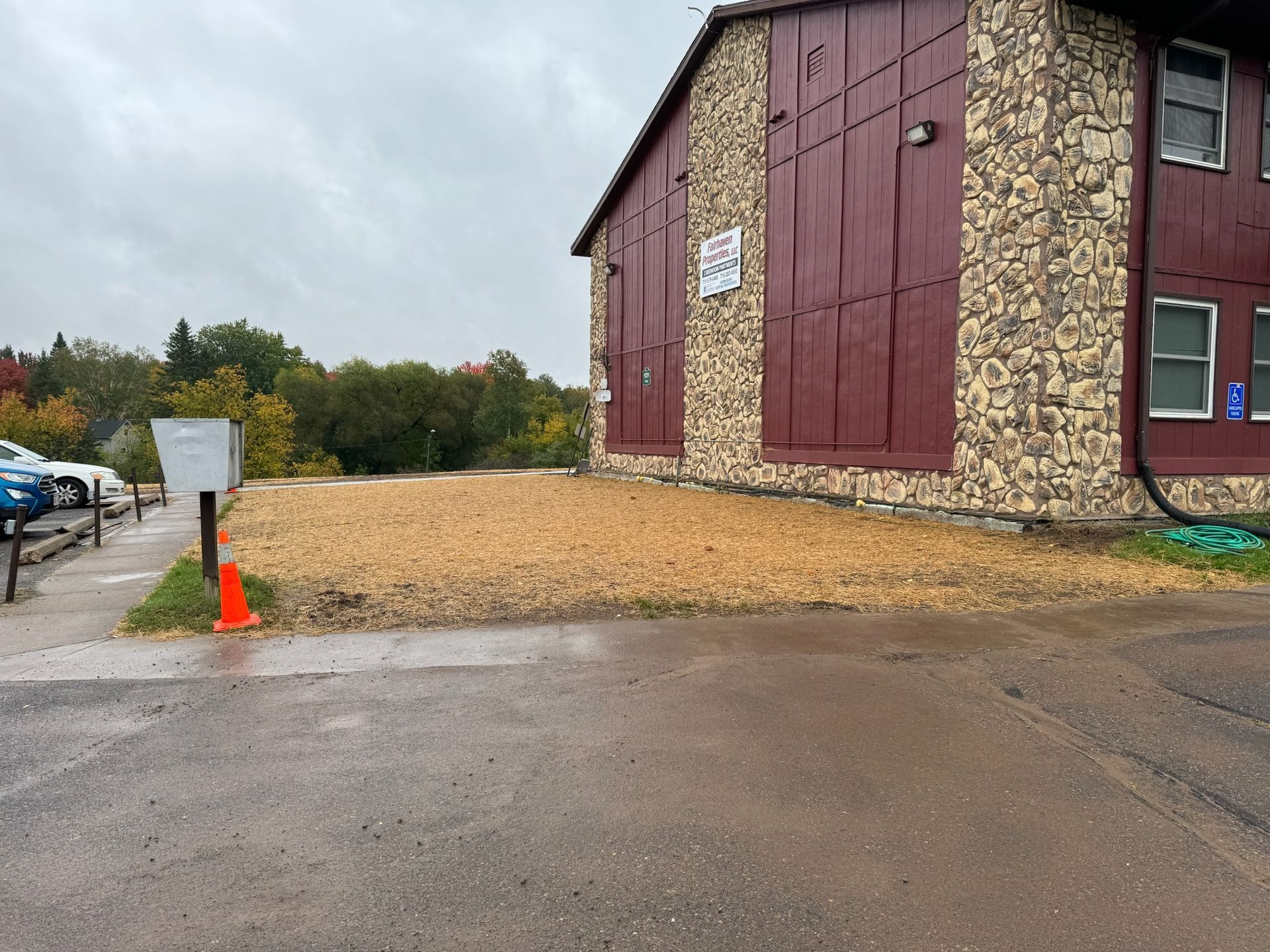 Exterior of a building with stone siding and a red door.  A bare dirt patch is in front of the building.