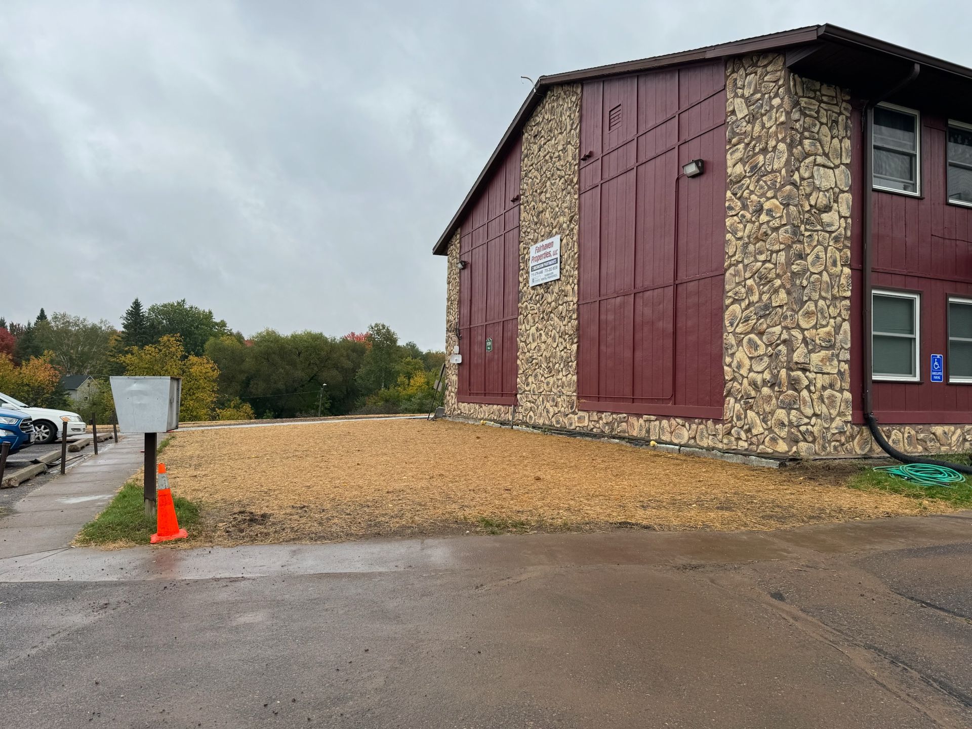 Building exterior with reddish siding, tan stone, and a mail box. Area in front covered with wood chips.