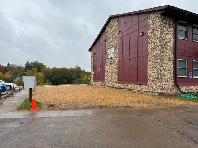 Building with stone and red siding. A bare patch of ground sits in front. Overcast day.