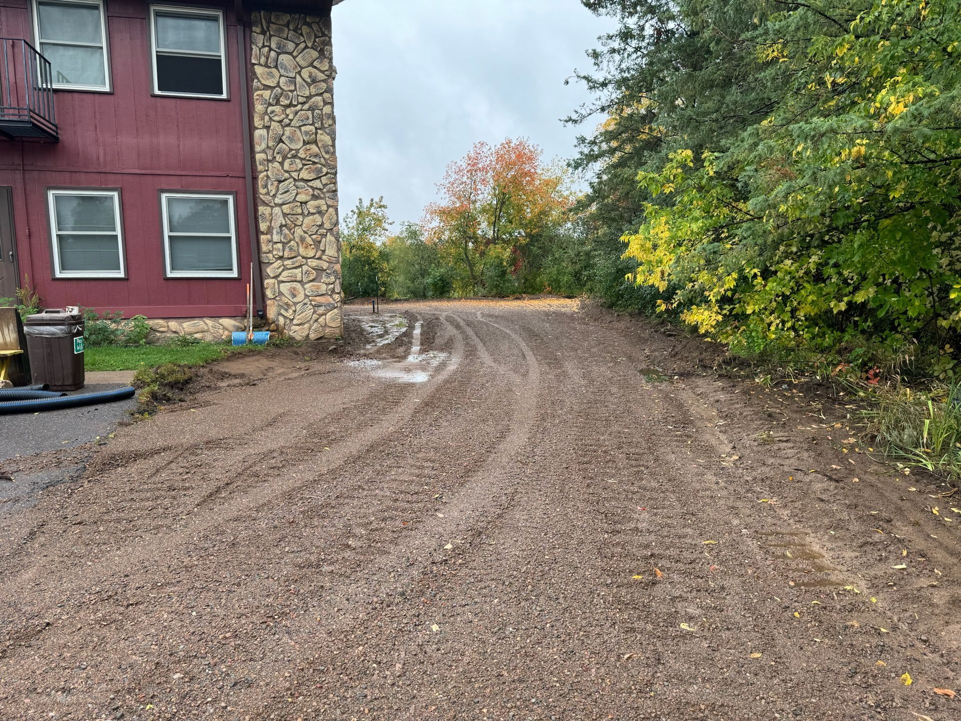 Gravel driveway leading up to a two-story red building with brown stone facade, surrounded by trees under an overcast sky.