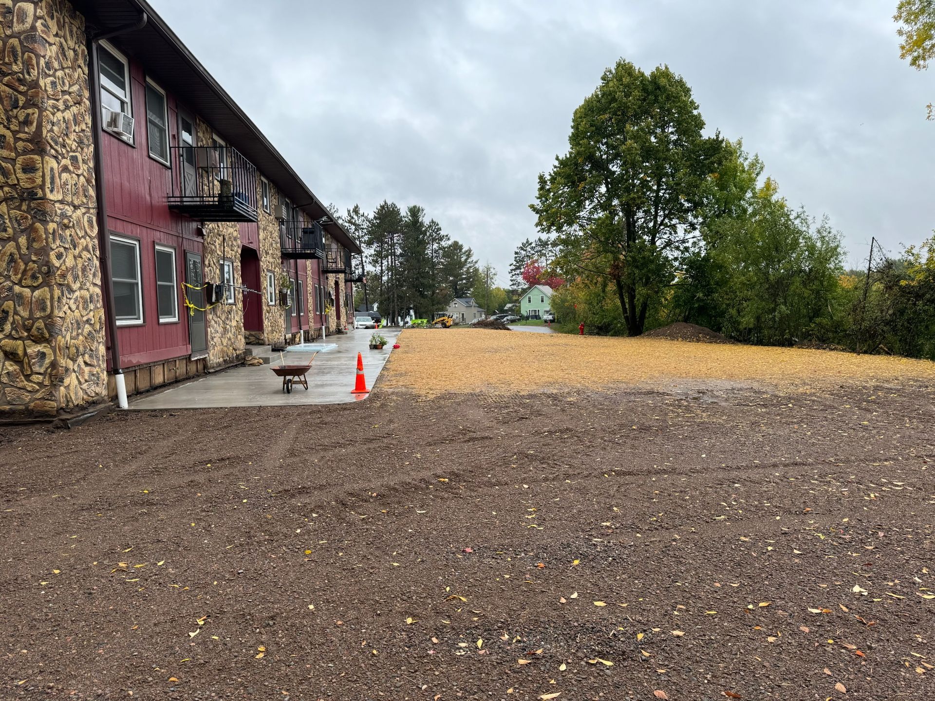 Exterior of a two-story building with a rocky facade and red siding. Brown gravel parking area.