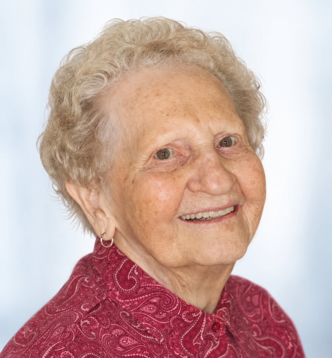 Elderly woman with beautiful natural smile, short gray hair and red blouse against blue background.