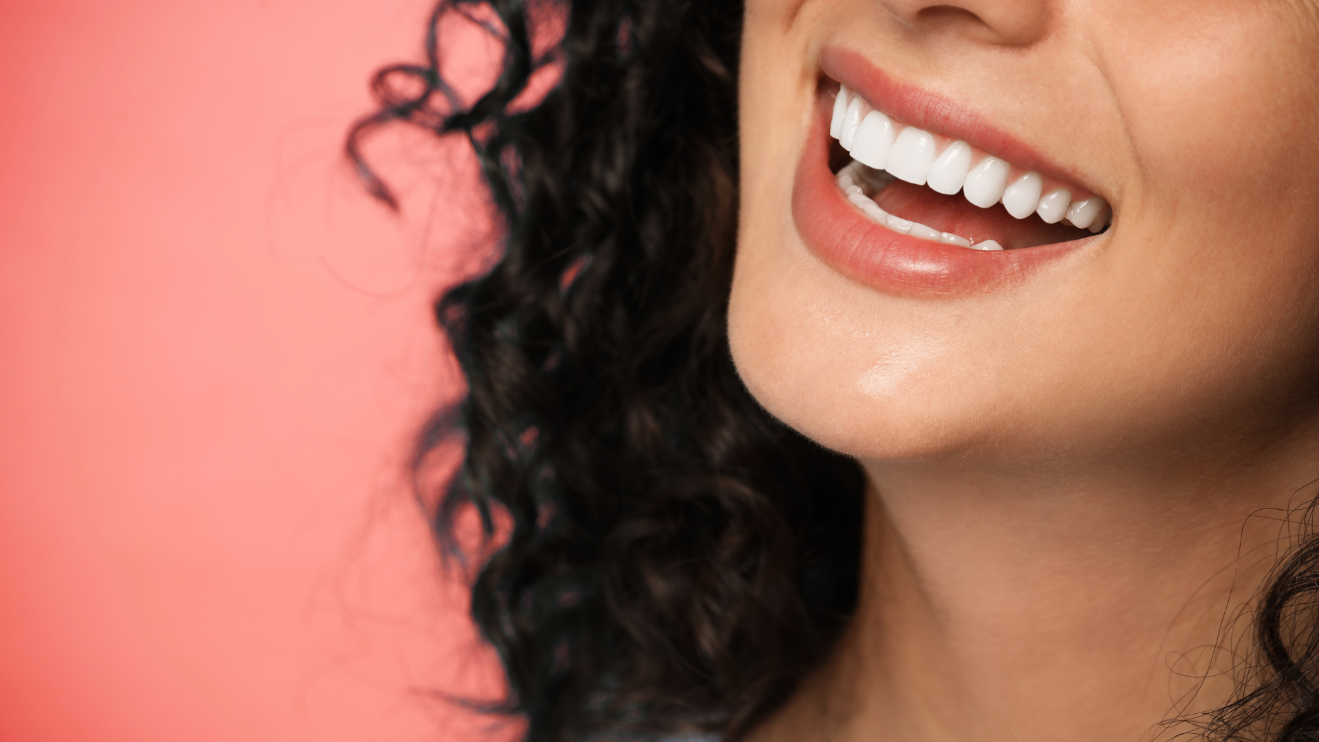Smiling mouth and lower face with curly dark hair against a pink background