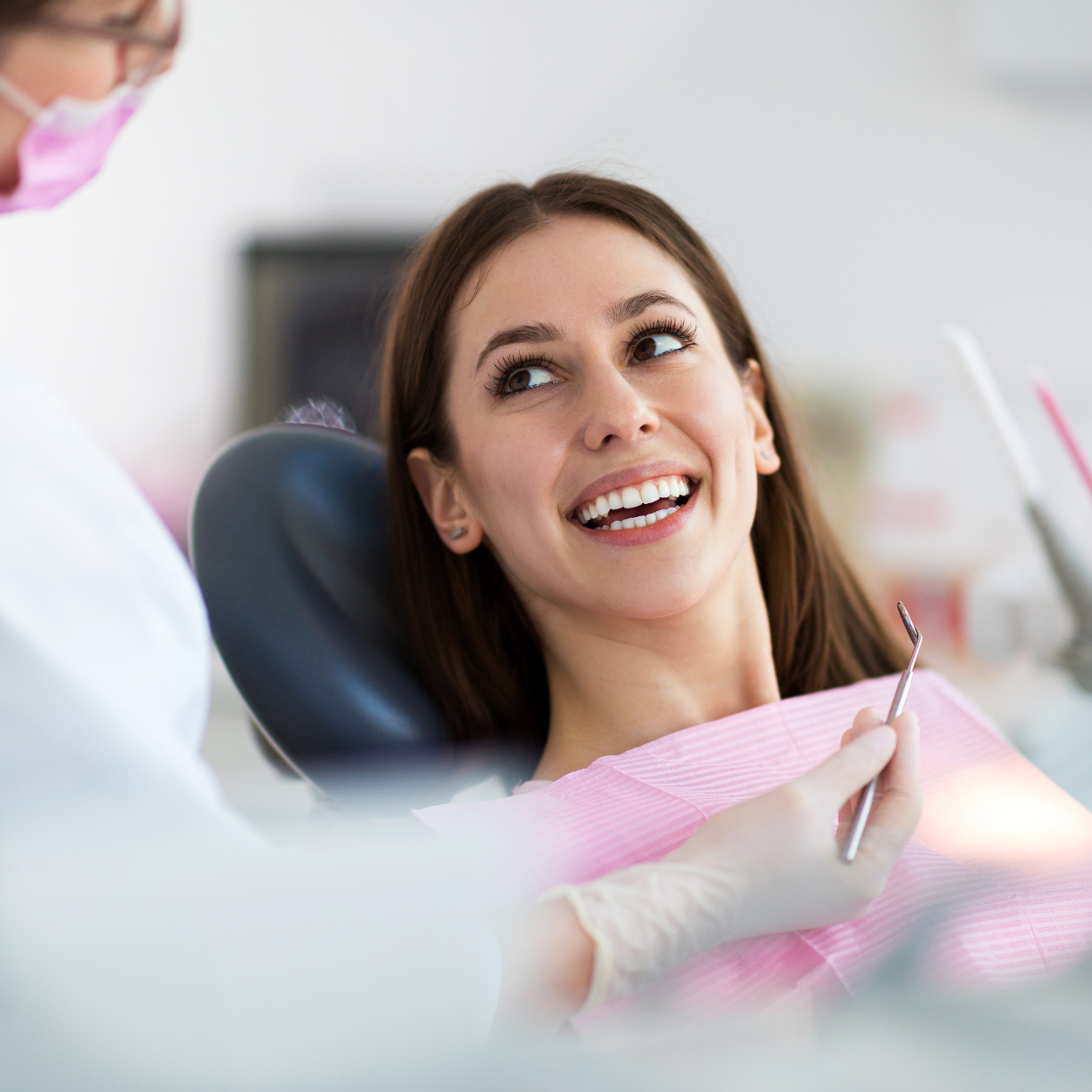 Smiling patient in a dental chair, looking up at a dentist holding tools.