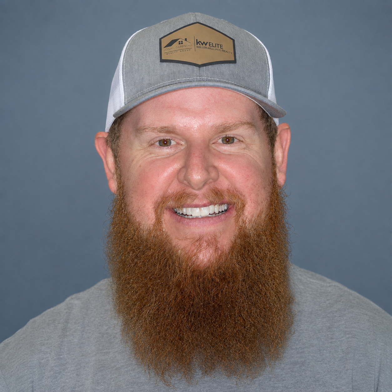 Smiling person with a long beard wearing a gray cap and gray
 shirt in a bright room