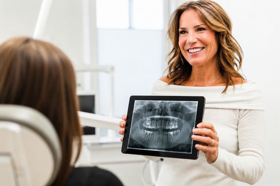 Woman in white shirt holding a dental X-ray and smiling in a clinic