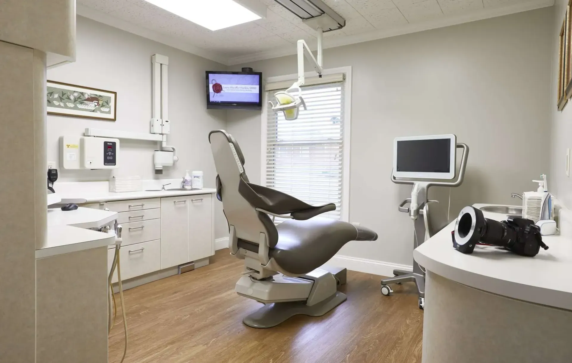 Empty dental exam room with a reclining chair, monitor, cabinets, and medical equipment