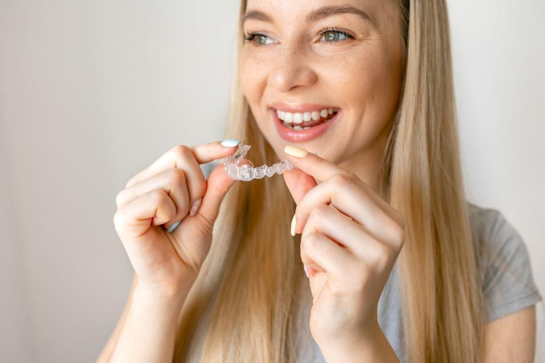 Smiling woman holding a clear dental aligner near her mouth in a bright indoor setting
