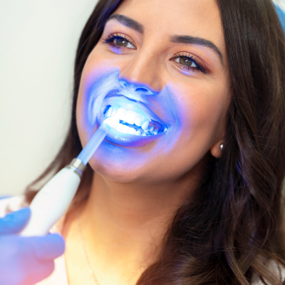 Woman receiving blue LED teeth whitening treatment with a handheld device