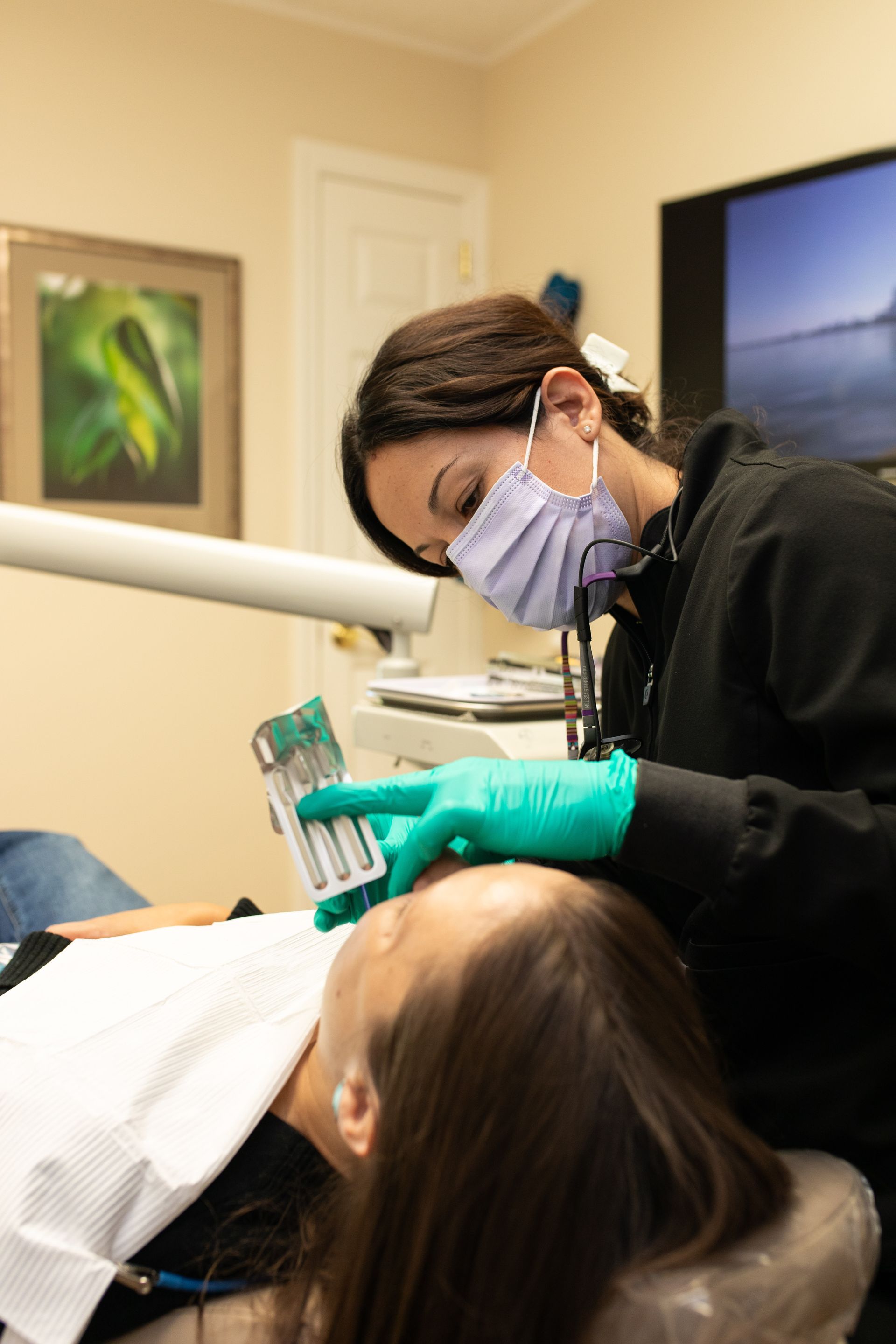 Dentist in mask and gloves treating a reclining patient in a dental office