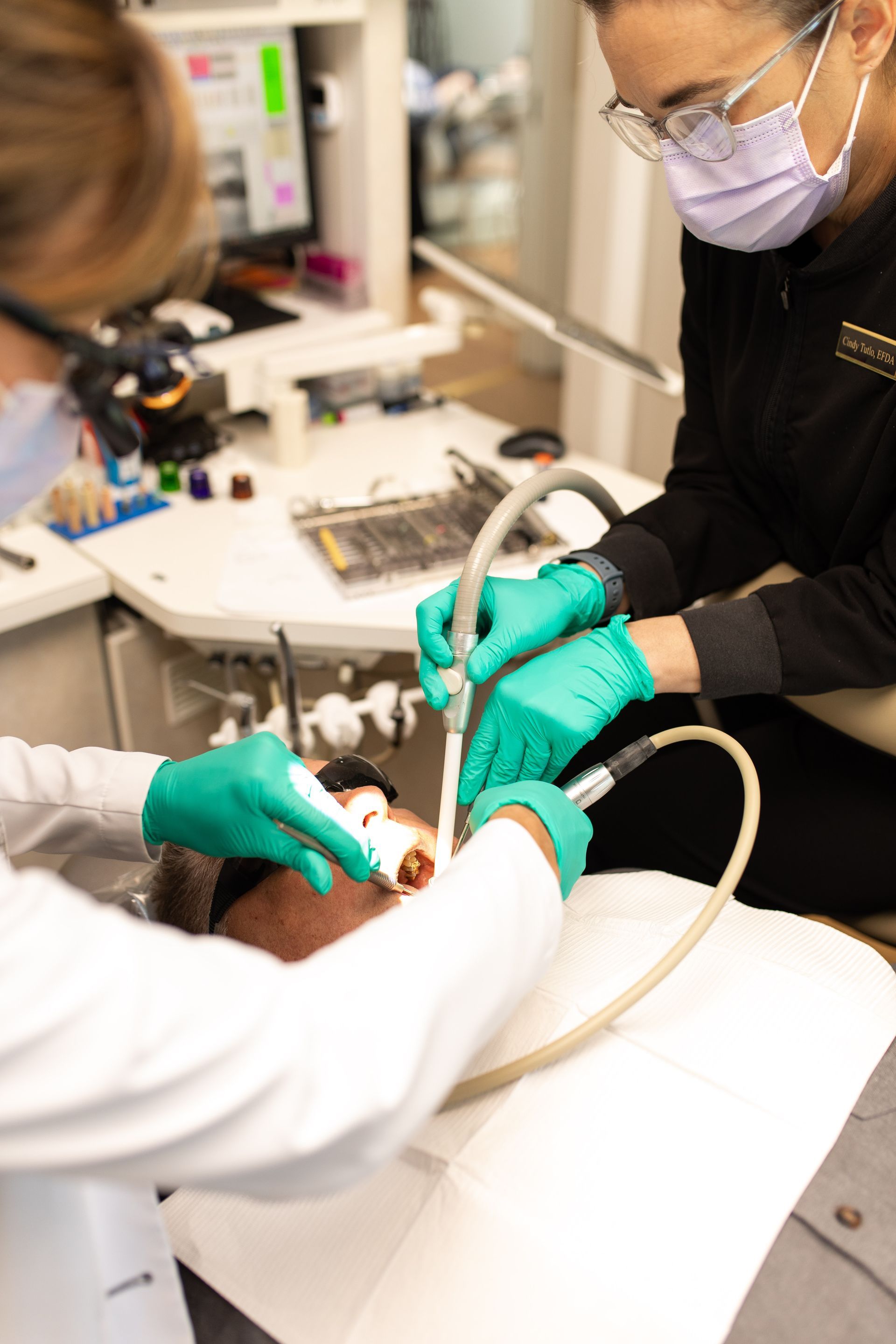 Dentist and assistant treating a patient with dental tools in a clinic, wearing masks and green gloves